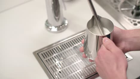 Top-view-of-milk-frothing-and-spinning-cream-in-silver-cup-at-clean-white-cafe