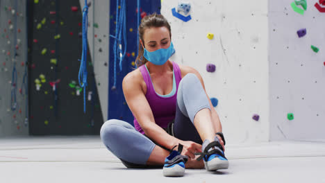 Mujer-Caucásica-Con-Mascarilla-Poniéndose-Zapatos-De-Escalada-En-La-Pared-De-Escalada-Interior