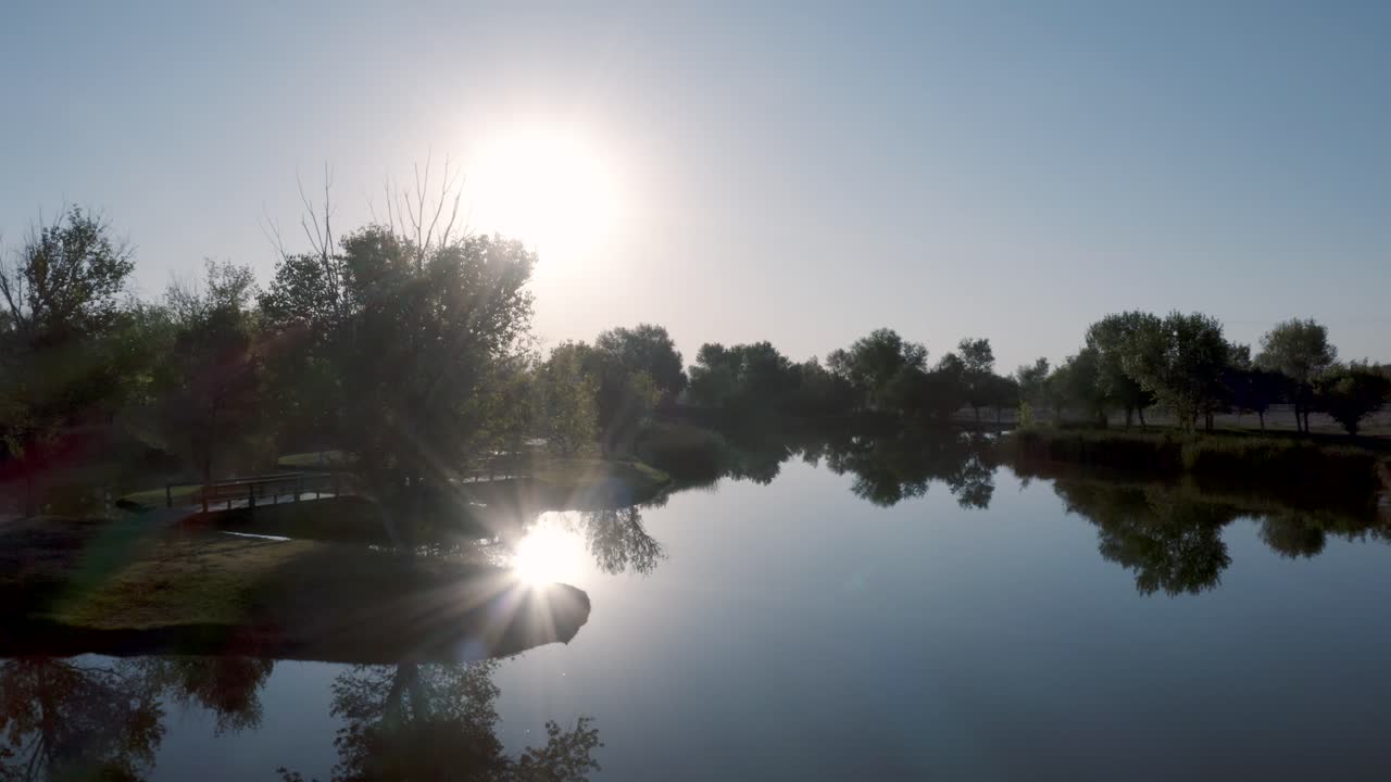 sol brillando sobre un plácido lago azul bordeado de árboles al amanecer, antena