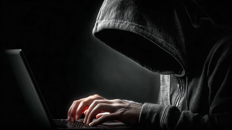 Una figura misteriosa incappucciata si concentra intensamente sullo schermo mentre digita su un laptop in un ambiente buio, incarnando l'essenza della segretezza e dell'intrigo guidato dalla tecnologia