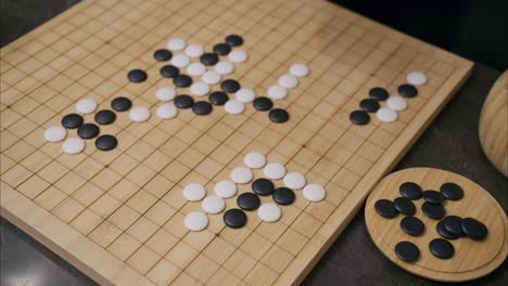 ángulo superior de 45 grados de la mano jugando piedra blanca en el juego de mesa de go con azulejos ya en la cuadrícula y piezas negras en la esquina