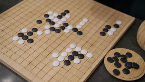 45 degree overhead angle of hand playing white stone in go board game with tiles already on grid and black pieces in corner