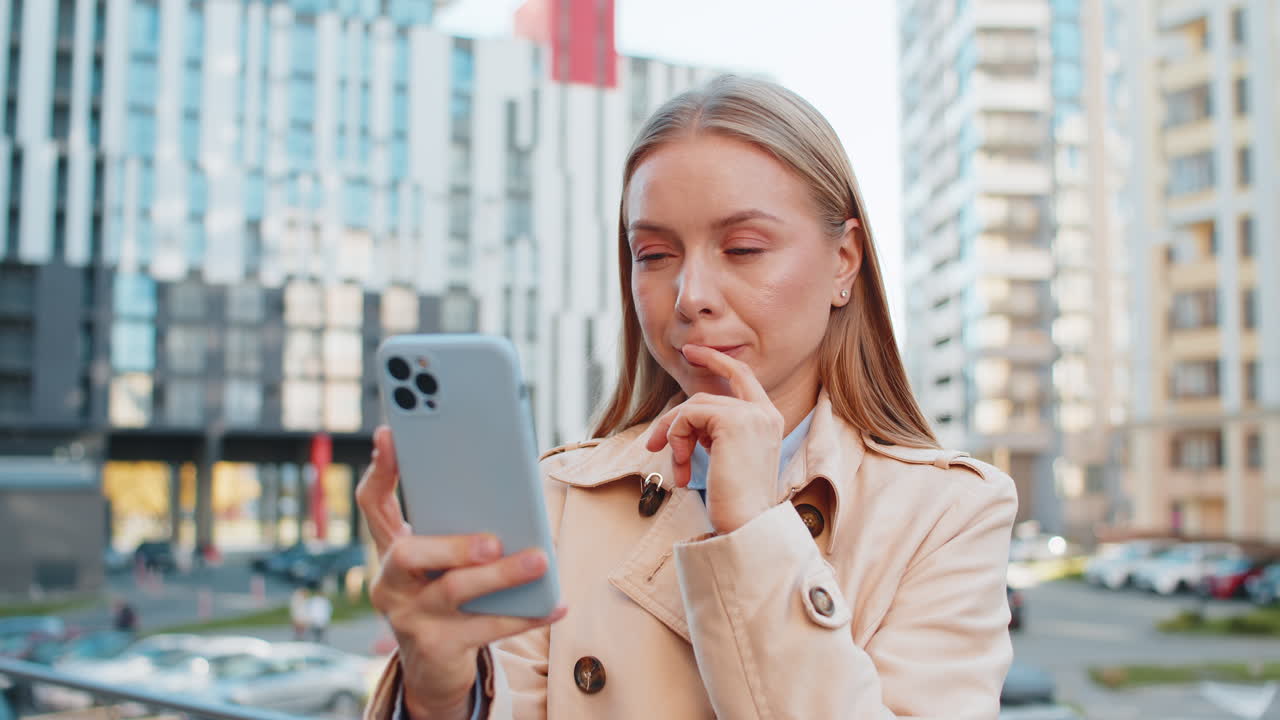 una mujer de negocios madura sonriente hablando en internet a través de un teléfono móvil de pie en la calle del centro de la ciudad