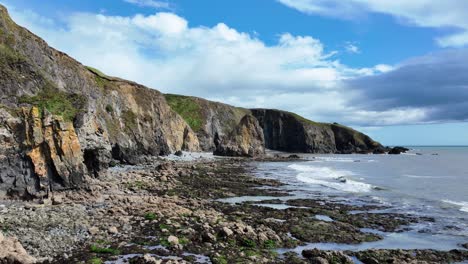 ireland epic drone flying slowly over rocky beach at low tide dramatic sea cliffs and beautiful sky waterford coastline on a bright summer morning