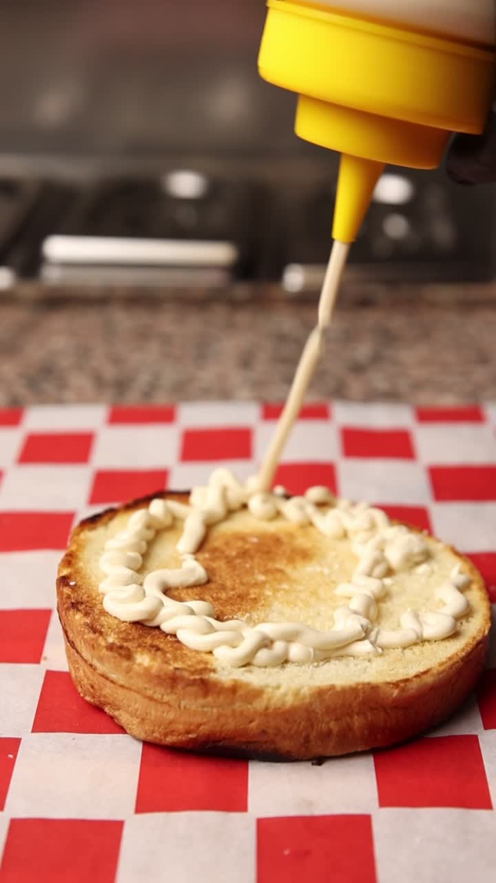Spremere la maionese su un panino tostato per hamburger per un sandwich