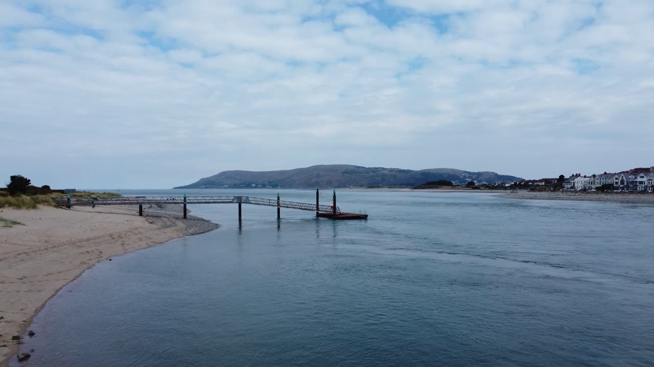 바다 경치를 가로질러 바라보는 경치 좋은 웨일스 산 해안 해변 부두를 향한 낮은 각도의 공중 전망 비행