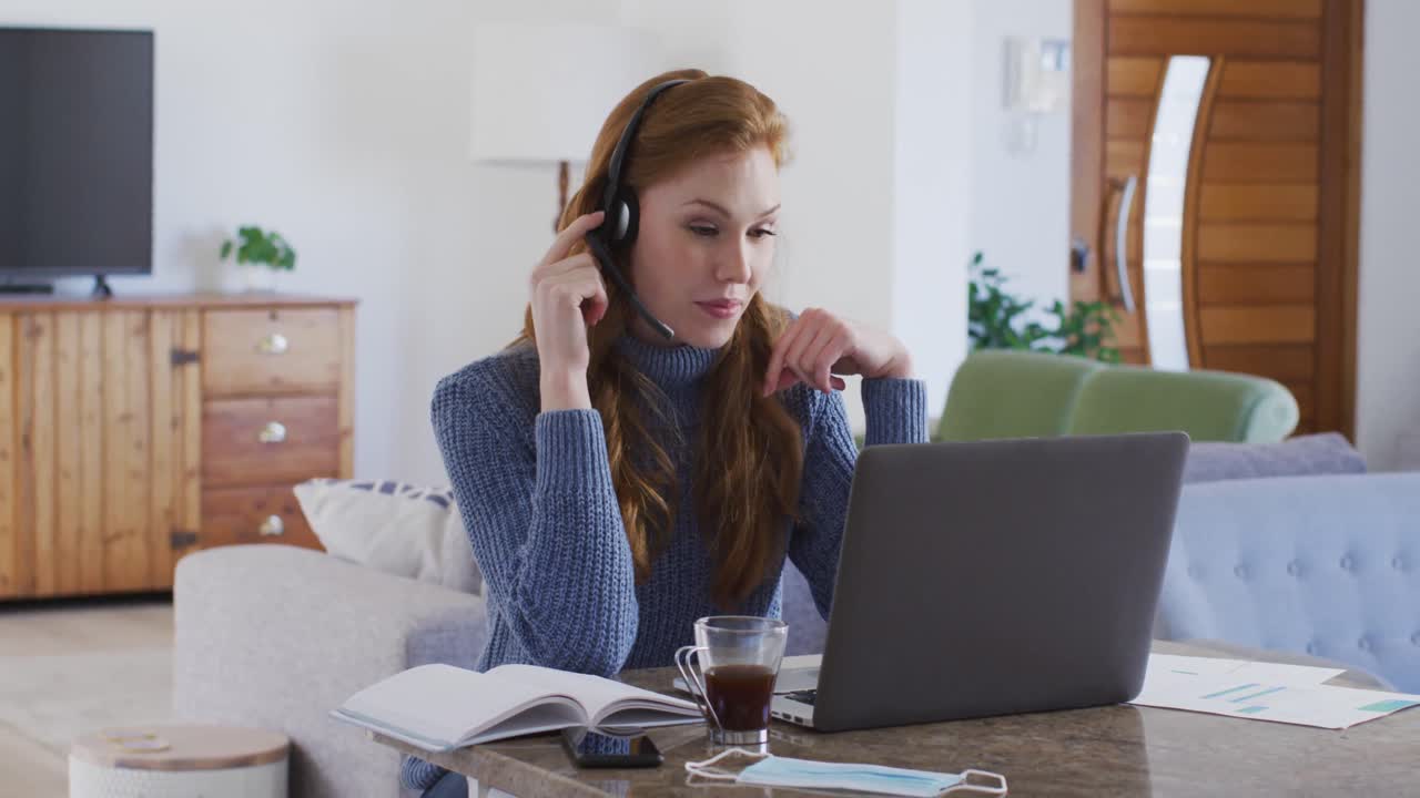 Kvinde med hovedtelefoner bruger laptop derhjemme.