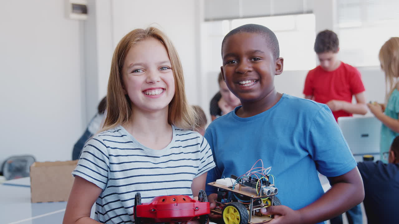 Portrait Of Male And Female Students Holding Robot Vehicle In After School Computer Coding Class