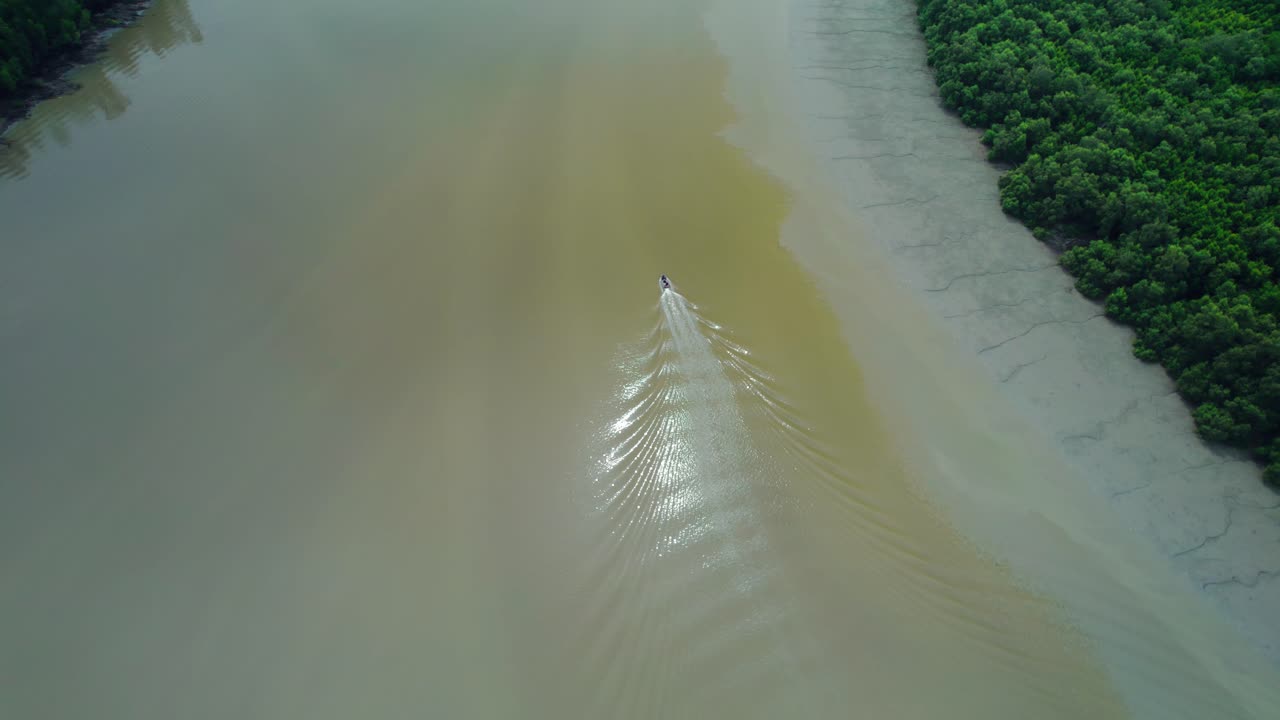 Drone footage of a vessel moving along river waters with rippling patterns and marshlands