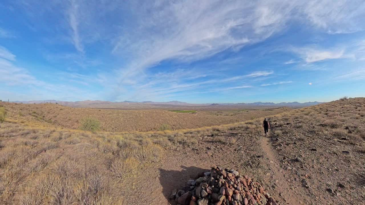 Pan over a hill as a senior woman walks down hill in McDowell Mountain Regional Park.