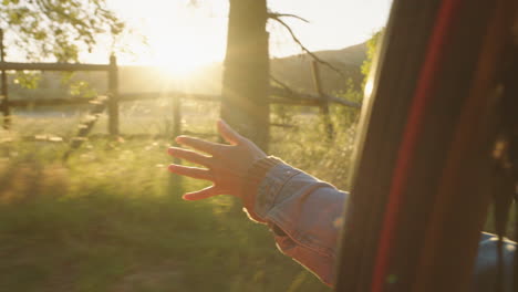 mujer en el coche con la mano afuera de la ventana sintiendo el viento soplando a través de los dedos conduciendo en el campo viajando en vacaciones de verano viaje por carretera disfrutando de la libertad en la carretera al atardecer