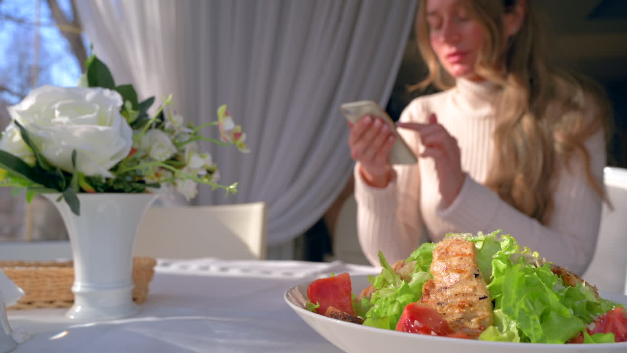 Woman scrolling on her phone at a table with white flowers and a salad at a restaurant