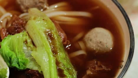 a close-up of a rich noodle soup featuring meatballs, fresh lettuce, and a savory broth.