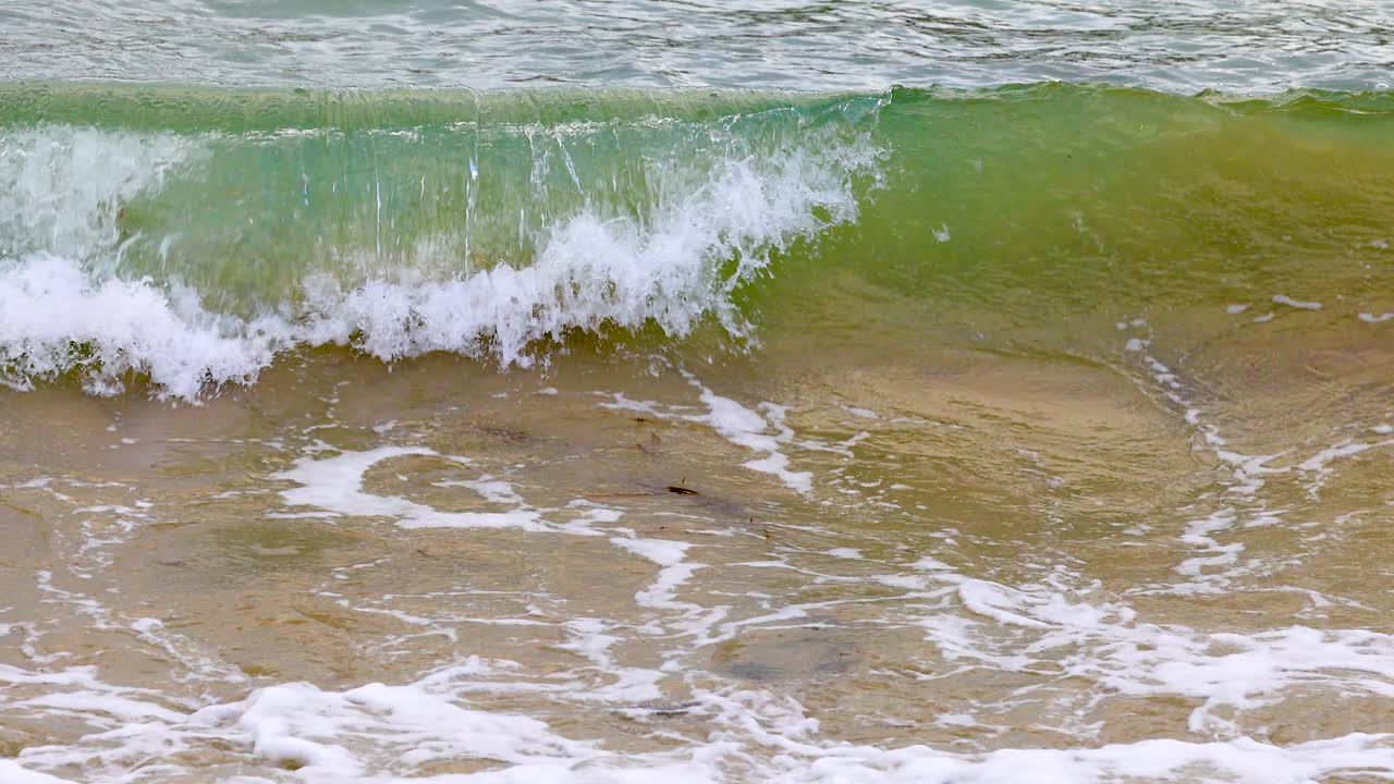 Dynamic ocean waves crash onto the sandy shore at Port Campbell, Australia, captured in natural daylight with vibrant green hues