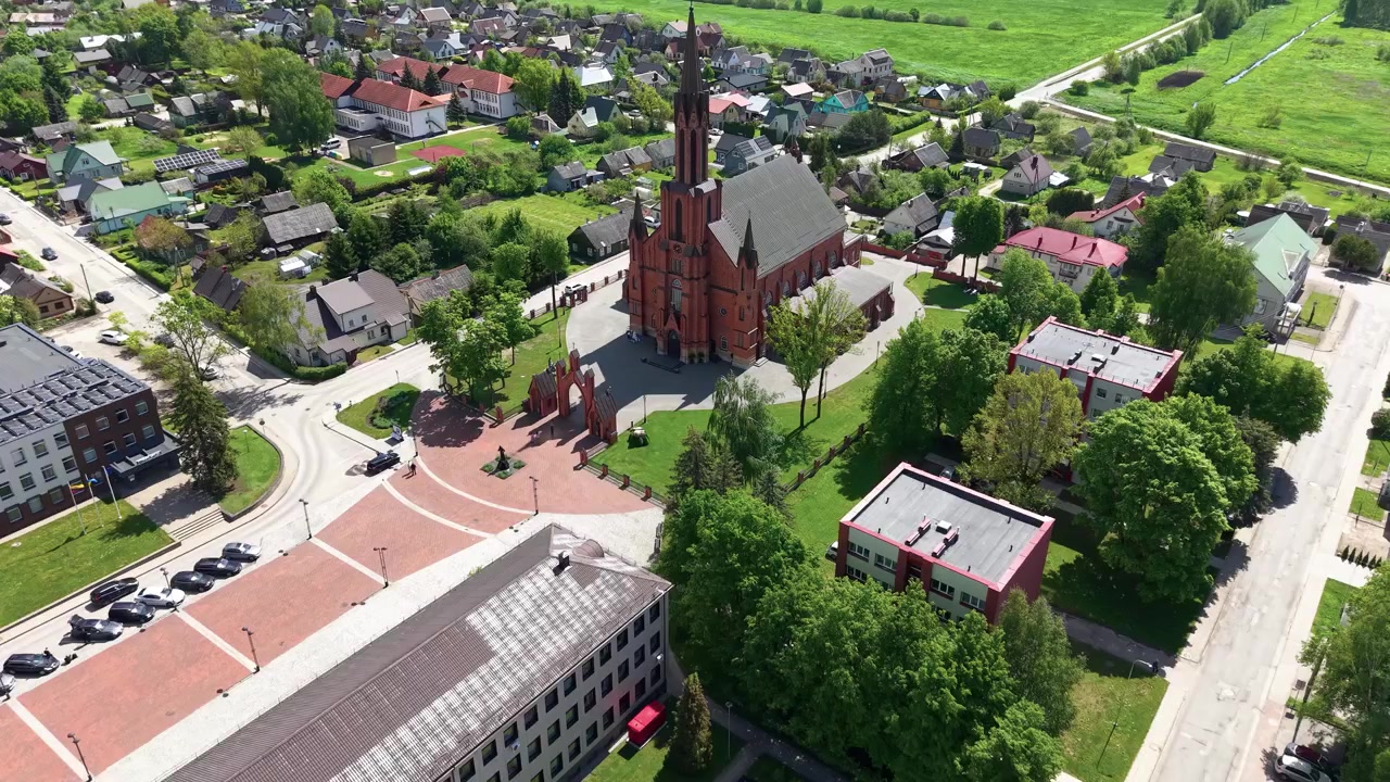 Ohromující letecké záběry katedrály Kaišiadorys a okolních budov v Litvě, zachycené za jasného slunečného dne. Živá zeleň, čisté ulice a nápadná architektura z červených cihel vyplňují scénu.