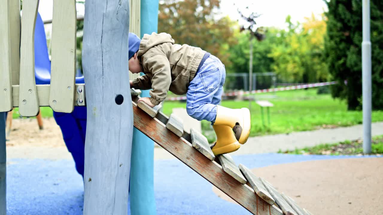Ein kleiner, 2-jähriger Junge rennt und spielt im Herbst auf dem Spielplatz. Ein Kleinkind ist draußen im Park auf dem Spielplatz unterwegs.