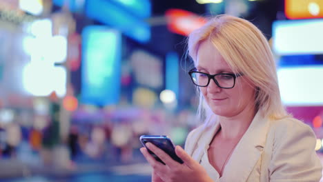 mujer de negocios usa un teléfono inteligente en el contexto de las luces publicitarias de los tiempos famosos