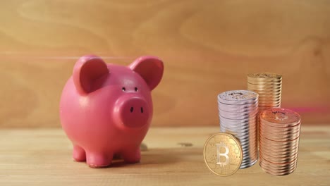 stack of coins over coins falling on pink piggy against wooden background.