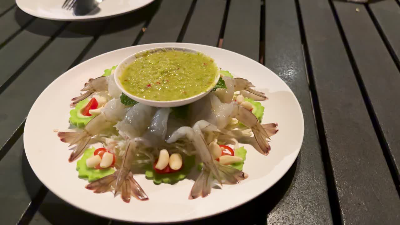 Raw shrimp arranged around spicy green sauce, outdoor dining table, evening lighting, slow camera movement