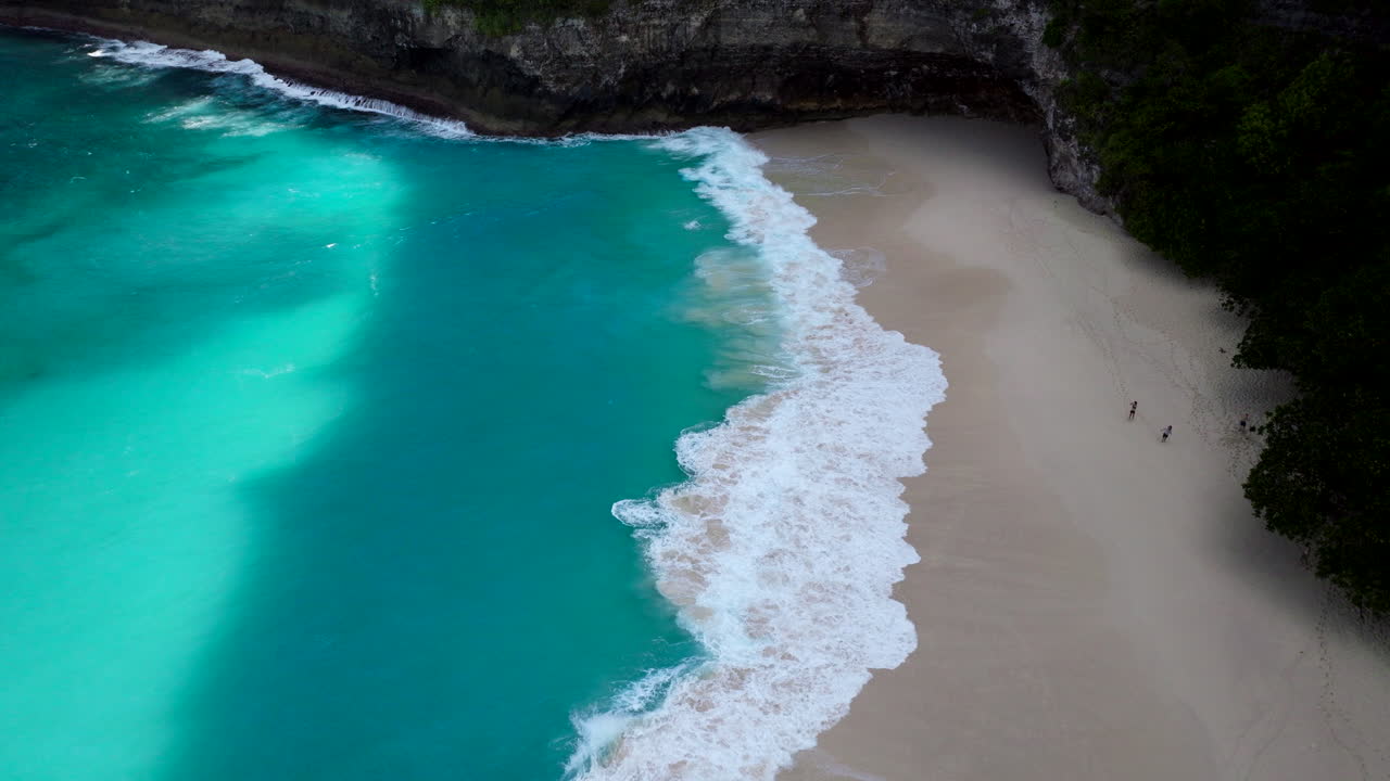 Piccole persone stanno sulla sabbia dorata della spiaggia di Kelingking mentre le onde si infrangono sulla riva