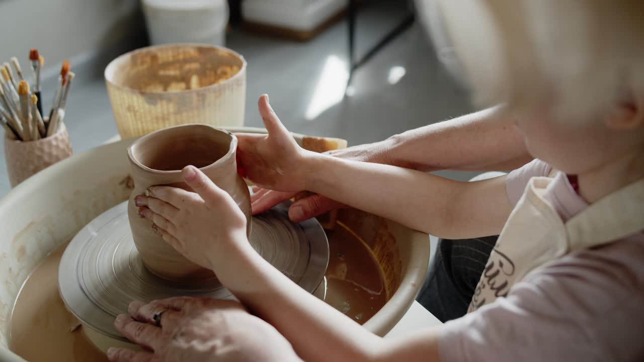 Grandmother teaches her granddaughter working on a pottery rotating wheel