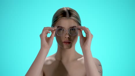 disparo estático medio de una joven mujer bonita quitando sus gafas y mirando a la cámara frente al fondo turquesa en cámara lenta