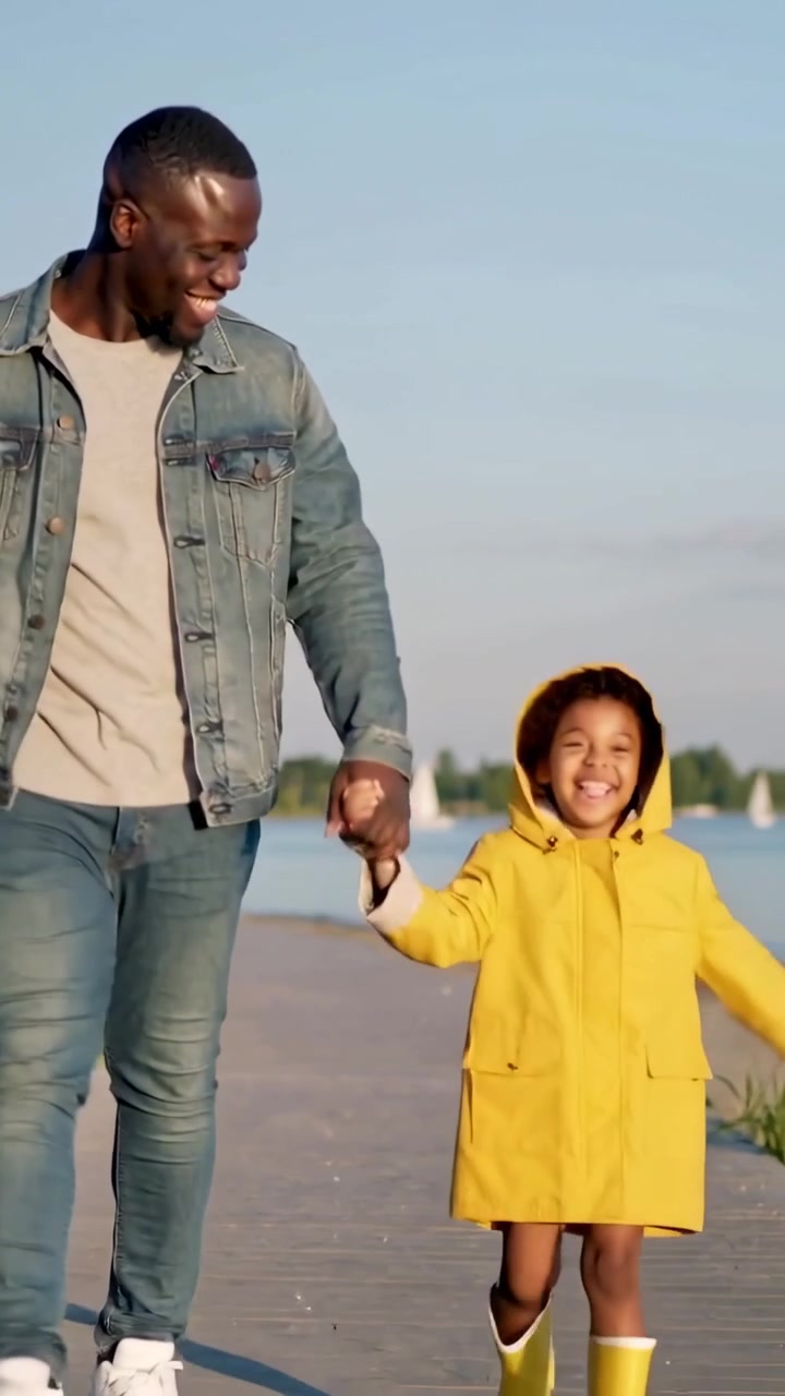 Video verticale: Uomo e bambina che camminano mano nella mano su una passerella, entrano da sinistra con cappotto giallo