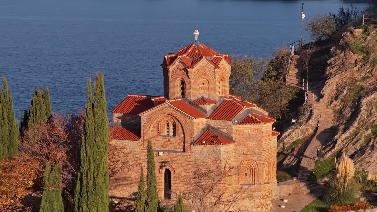 Vista aerea con drone dell'iconica chiesa di San Giovanni Teologo arroccata sul lago di Ocrida, incorniciata da cipressi e colori autunnali. Macedonia del Nord