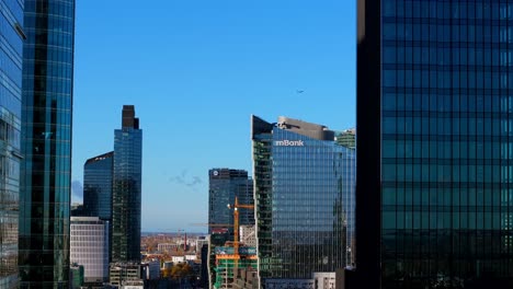 aerial view of airplane flying above warsaw poland, financial center towers and buildings on sunny day, parallax drone shot
