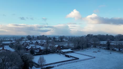 a drone shot captures a peaceful english village, its snow-covered rooftops glowing under the bright winter sun.