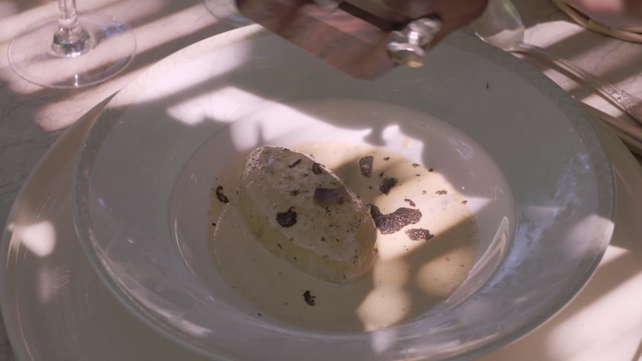 close-up shot of a dish in Provence, France, with sliced black truffles and a creamy sauce, being garnished with additional truffle shavings.
