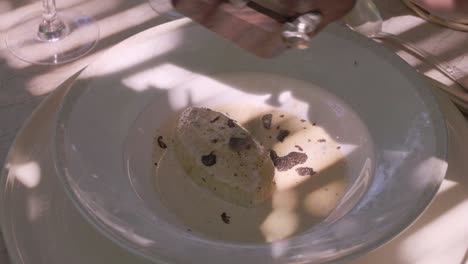 close-up shot of a dish in provence, france, with sliced black truffles and a creamy sauce, being garnished with additional truffle shavings.