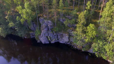 Beautiful-drone-footage-of-rocky-shoreline-of-a-forest-lake-in-the-borealis-wilderness-in-Finland