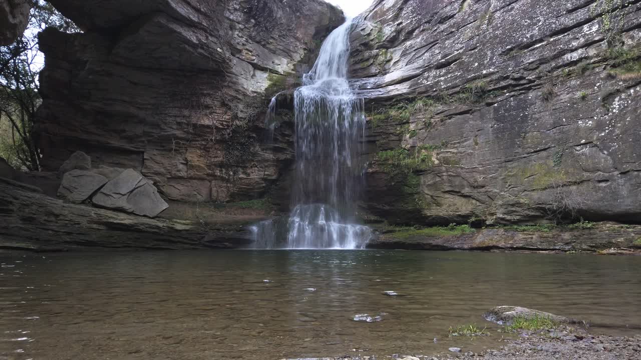 Cascading water falling from moss covered rocky cliffs, forming crystal clear pond within serene natural park landscape in les guilleries, catalonia, spain