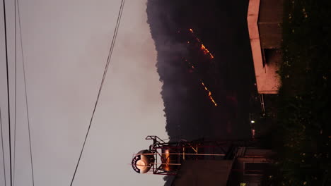 Wildfire-spreading-in-Vietnam-jungle-near-small-town,-vertical-video