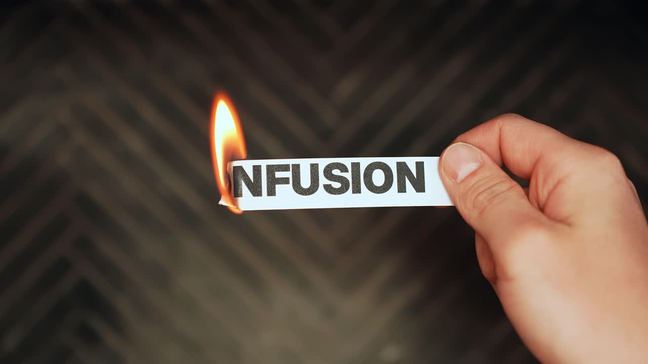 Close-up of a hand holding a paper strip labeled “CONFUSION” as the edge burns with flame on a dark background. Mental clarity and overcoming uncertainty concept with copy space