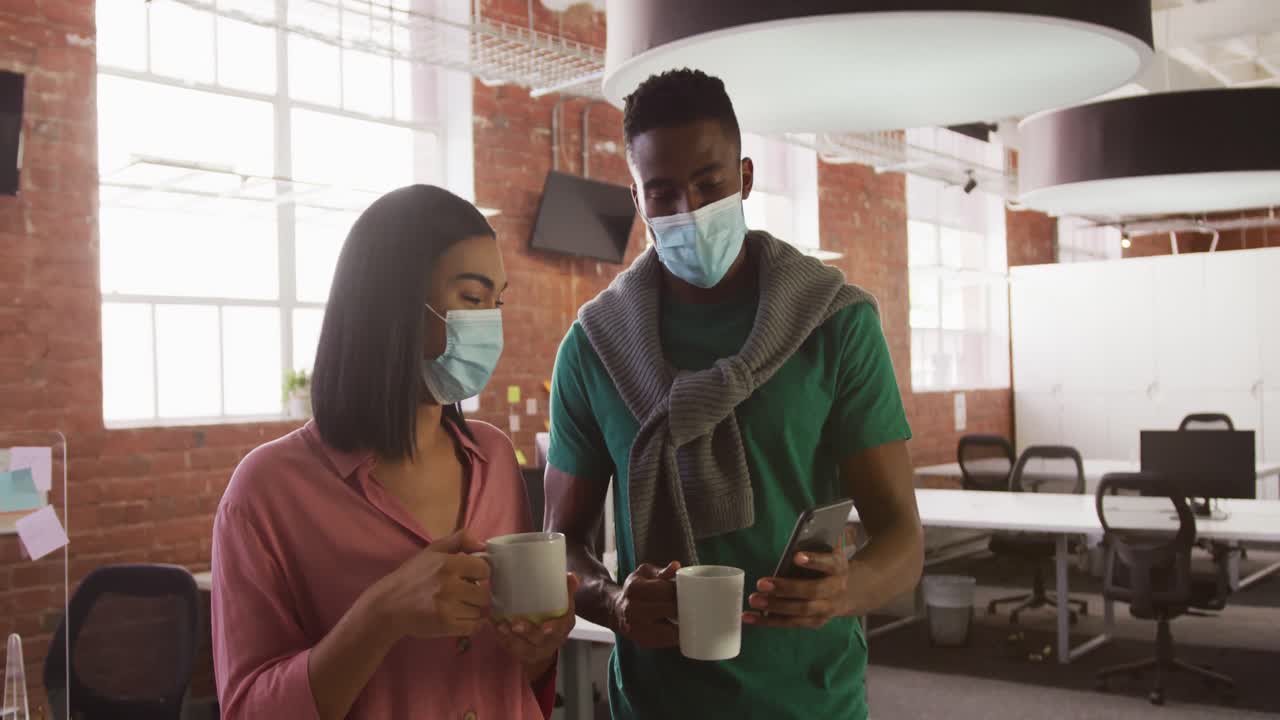 Diversi colleghi e colleghe d'affari che indossano mascherine, usano smartphone e tengono in mano tazze.