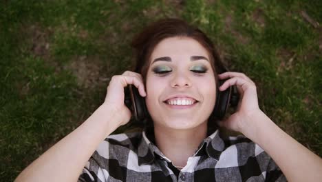 auriculares en las manos femeninas. chica encantadora acostada de espaldas en la hierba, poniéndose los auriculares y escuchando con placer la música. disparando desde arriba