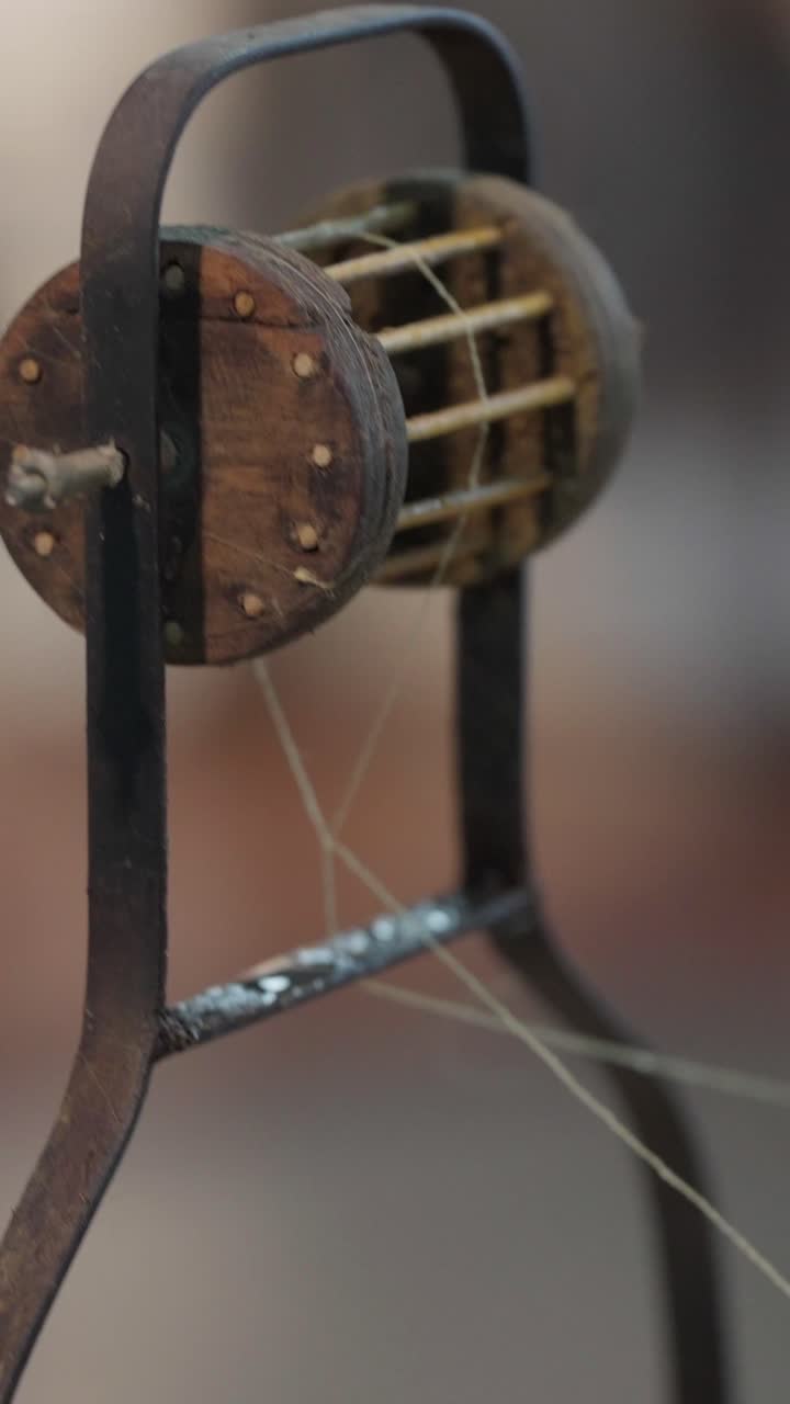 Close shot of a traditional wooden silk reeling wheel spinning while a worker hand pulls delicate silk threads from boiled cocoons in Thailand slow motion natural textile craft