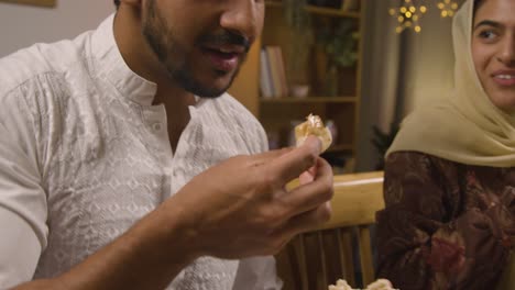 familia musulmana sentada alrededor de una mesa en casa comiendo para celebrar el eid 1