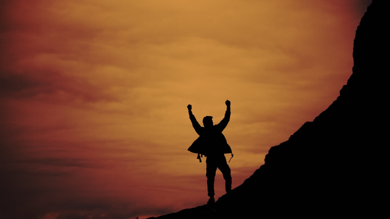 Silhouette of a man celebrating success on a mountain peak at sunset