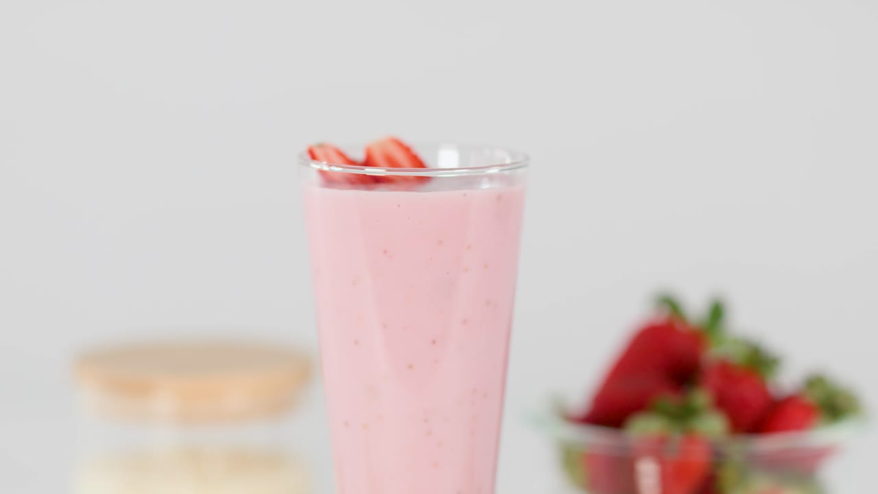 Una mano introduce una pajita roja en espiral en un cremoso batido de fresa rosa bajo una iluminación de estudio brillante
