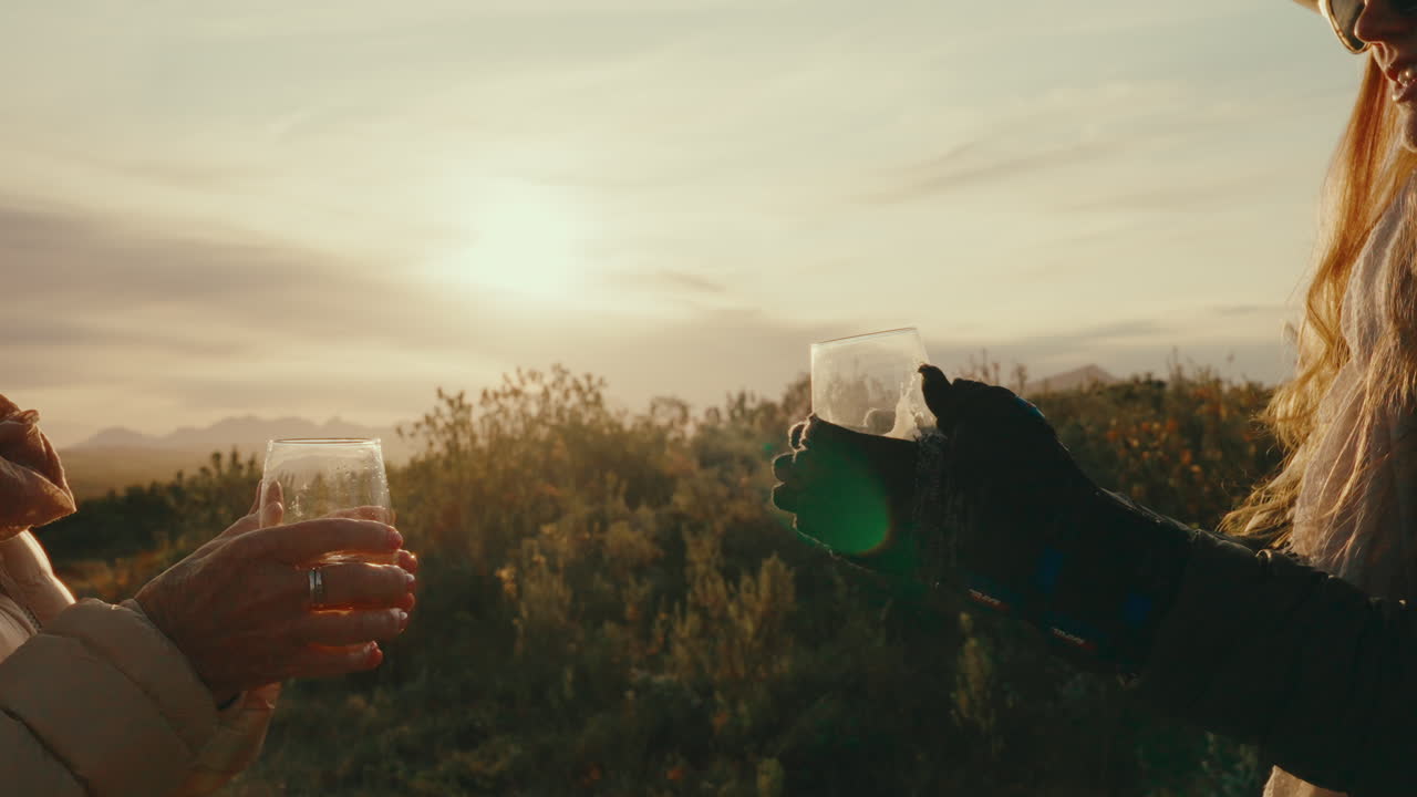 Glassware cheers between two friends at sunset on luxury travel trip, toasting wine or cocktails in 4k push in slow motion