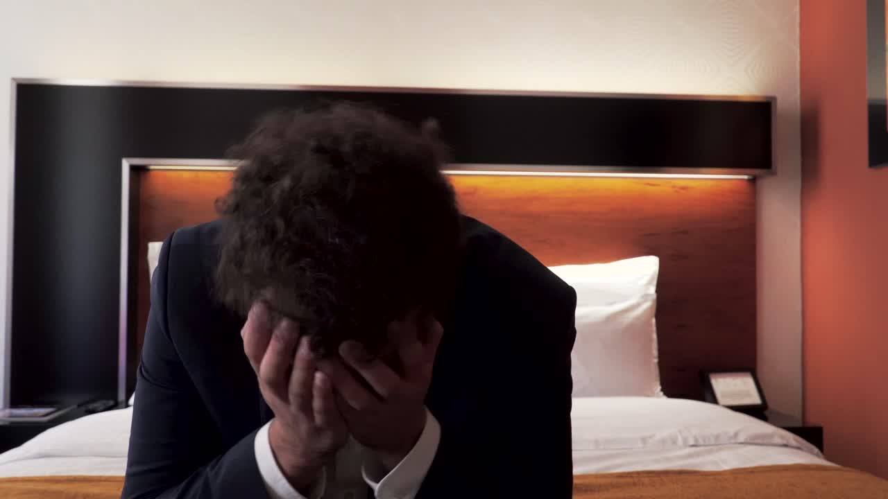 Male business traveler frustrated and shaking head on bed in hotel room
