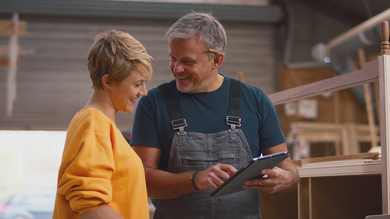 apprendista femminile che impara da un falegname maschio maturo con un tablet digitale in un laboratorio di mobili