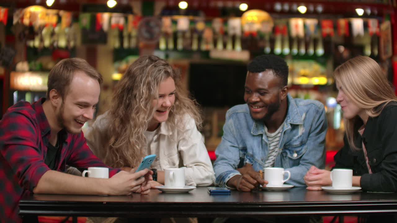 A man shows his friends funny vines on his smartphone. A company of friends discusses photos and videos while looking at the phone screen a multi-ethnic multinational company of four friends.