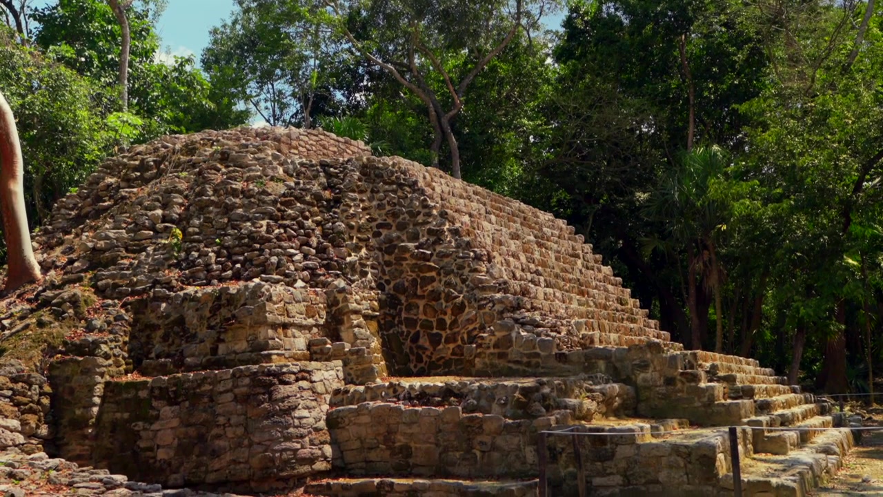 Un'affascinante ripresa in tilt-down rivela l'antica piramide di Oxtankah che emerge dalla lussureggiante giungla verde in una splendida giornata di sole in Messico.
