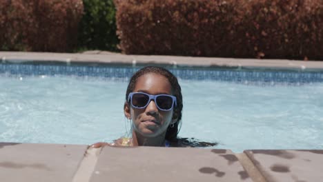 portrait of happy african american girl wearing sunglasses in swimming pool, slow motion