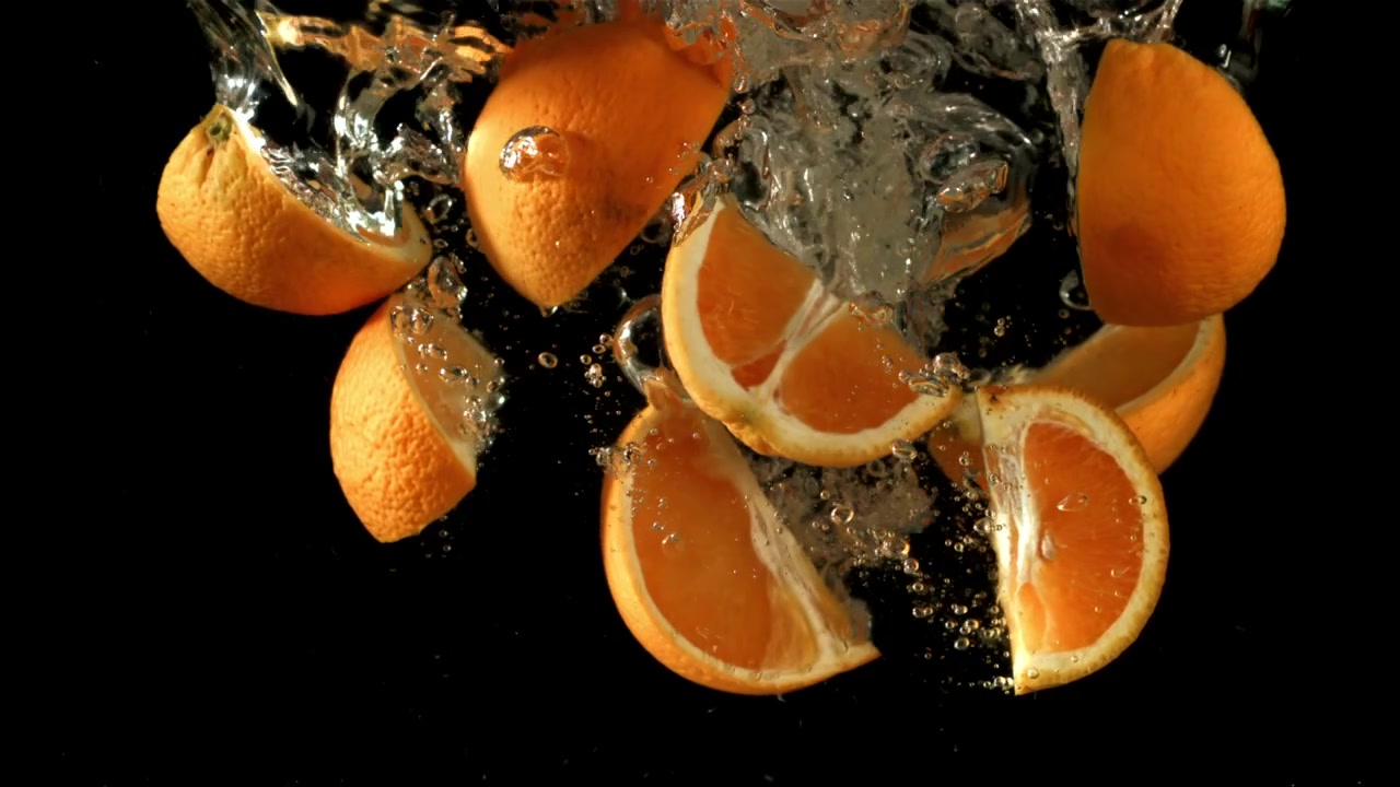 Fette e mezze arance fresche che schizzano nell'acqua al rallentatore