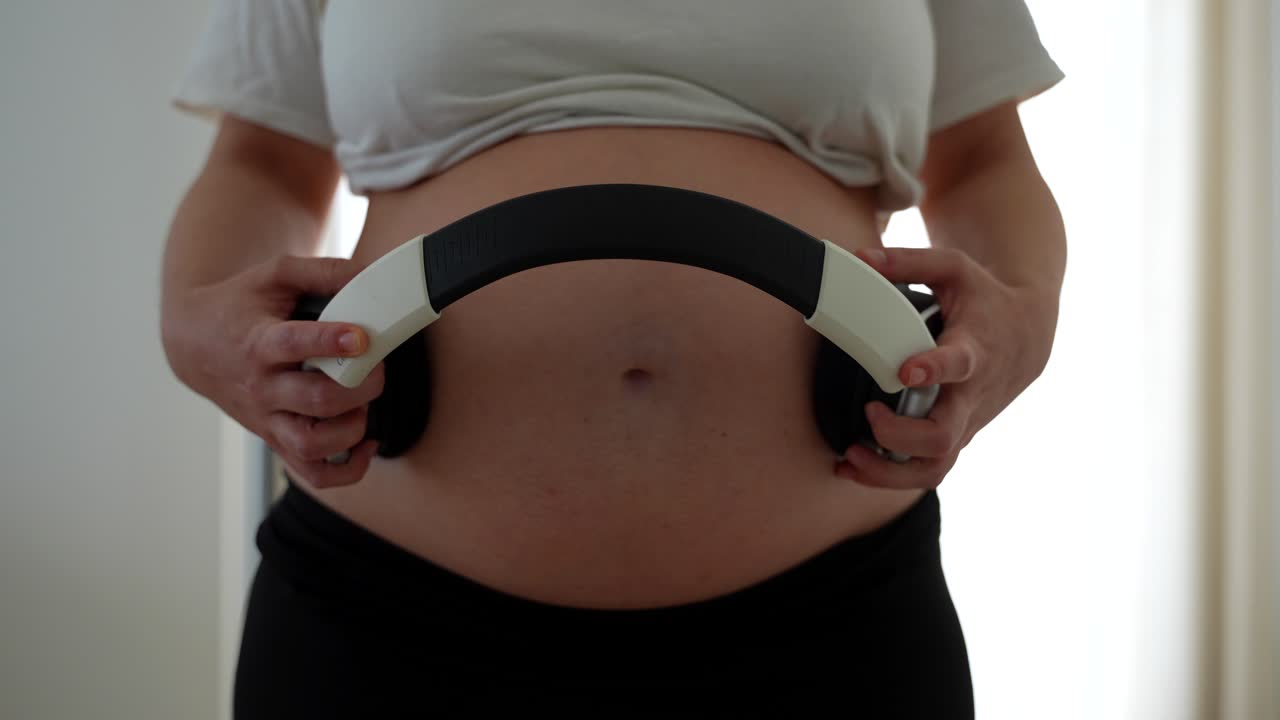 Pregnant woman uses headphones on belly to play calming music for unborn baby
